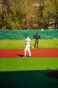 Baseball player fielding on a vibrant turf, with an umpire observing in the background on a sunny day.
