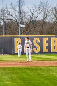 Two baseball players on the field with Tigers in the background during a game at a sports complex.