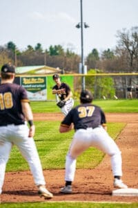 A baseball player on the mound prepares to pitch while teammates stand ready on the field. Bright sunny day.