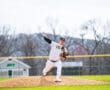 Baseball pitcher in striped uniform delivers a pitch from the mound on a sunny day at the ballpark.