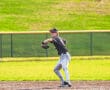 A young baseball player prepares to throw, wearing a black jersey and cap, on a sunny day at the field.