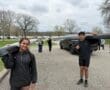 Two young rowers carrying a boat at a lakeside park, preparing for a team practice on a cloudy day.