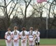 Softball players stand in formation, honoring the flag on the field before the game. Team spirit and respect shine.