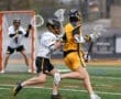 Lacrosse players compete on a field, one in yellow being pursued by an opponent in white during an intense game.
