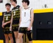 Three male volleyball players in team uniforms stand on the court, focused and ready for action during a game.