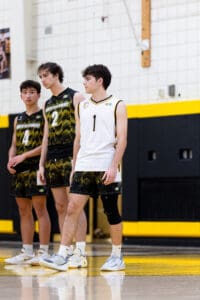 Three male volleyball players in team uniforms stand on the court, focused and ready for action during a game.