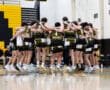 High school basketball team huddled together in celebration on the court, showcasing teamwork and camaraderie.