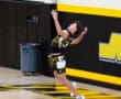 A young male athlete jumps to serve a volleyball in a gym, showcasing athleticism and focus during practice.