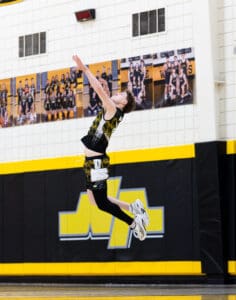 Young basketball player leaping for a shot in a gym with vibrant yellow and black team colors.