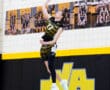 A volleyball player jumps to serve during a game, showcasing athleticism in a school gymnasium.
