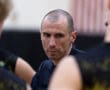 A focused coach speaks to players during a basketball practice, emphasizing strategy and teamwork.