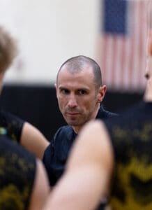 A focused coach speaks to players during a basketball practice, emphasizing strategy and teamwork.
