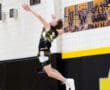 High school volleyball player jumping for a serve, showcasing athleticism against a gym backdrop.