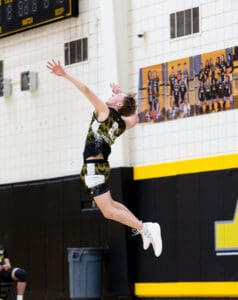 High school volleyball player jumping for a serve, showcasing athleticism against a gym backdrop.