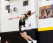 A volleyball player jumps to spike the ball during a match, showcasing athleticism in a gym environment.