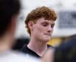 A focused basketball player with curly red hair participates in a team discussion on the court.