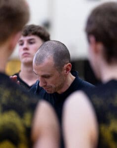 Coach discussing strategy with players during a basketball huddle, focusing on teamwork and preparation for the game.