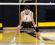 High school volleyball player in action stance, focused on the game, inside a gym with a yellow and black theme.