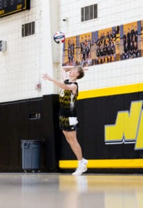 High school volleyball player serves during a match, showcasing athleticism and focus on the court.
