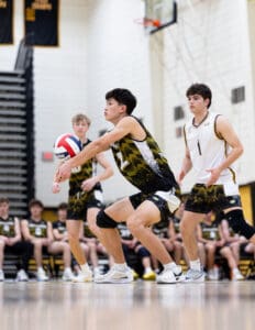 High school volleyball player prepares for a serve; teammates and spectators watch from the sidelines.
