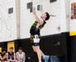 A volleyball player jumps to serve during a match, with teammates watching in the background.