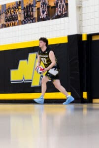 A volleyball player from North Allegheny prepares to serve during a game in a sports gymnasium.