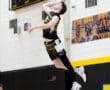 High school volleyball player jumps to serve the ball during a game, showcasing athleticism and concentration.