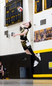 High school volleyball player jumps to serve the ball during a game, showcasing athleticism and concentration.