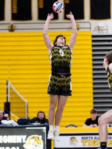 High school volleyball player jumps to set a ball during a match, showcasing skills in a vibrant gym.