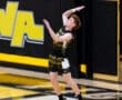 A volleyball player jumps to serve during a game in a gym with black and yellow colors.