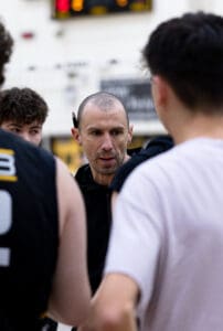 Coach instructing a basketball team during a huddle, emphasizing teamwork and strategy on the court.