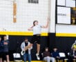 High school volleyball player jumping to hit a volleyball during a game, surrounded by spectators on the sidelines.