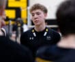A focused volleyball player in a black team jersey listening intently during a team huddle.