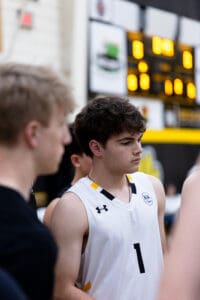 A focused basketball player in a white jersey stands among teammates during a game, capturing teamwork and concentration.