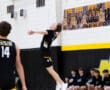 High school volleyball player serves the ball during a match, with teammates watching from the sidelines.