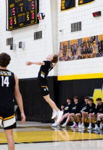 High school volleyball player serves the ball during a match, with teammates watching from the sidelines.