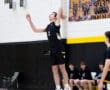 High school volleyball player jumping to serve during a match, teammates watching from the sidelines.