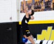 High school basketball player jumps to spike the ball during a game, showcasing athleticism in a gym setting.