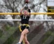 Girl in flag football gear jumps to catch a football, showcasing athleticism on a field with goalposts in the background.