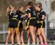 A group of female athletes in black uniforms discussing strategy during a flag football game on a sunny day.