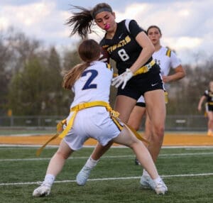 Two female athletes compete in a flag football game, showcasing dynamic gameplay on a grassy field.