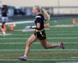 A female athlete runs on a field during a flag football game, showcasing determination and agility in action.