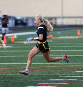 A female athlete runs on a field during a flag football game, showcasing determination and agility in action.