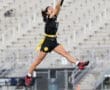Female athlete leaping to catch a flag football pass, wearing a black jersey and yellow flags on a football field.