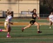 Action shot of two female athletes in a flag football game, one running with the ball and the other chasing her.