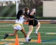 Two young girls playing flag football, one running with the ball while the other attempts to pull her flag.