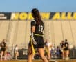 Female flag football player in black jersey, number 12, prepares for the game with North Allegheny stadium in the background.