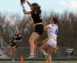 Girl in black jersey jumps to catch a football while another player in white attempts to block her during a game.