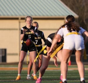 High school girls' flag football game with players in action on the field, one preparing to pass the ball.