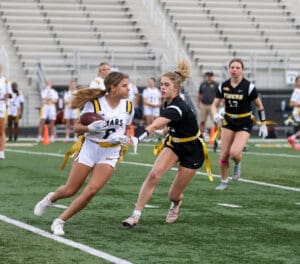 Girls playing flag football during a competitive match on a green field, showcasing teamwork and athleticism.